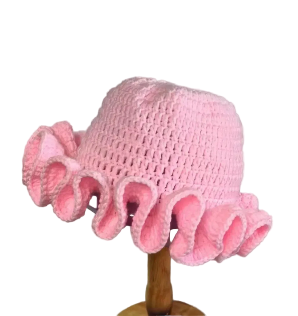 Pink knitted hat with ruffled brim on a wooden stand against a plain background